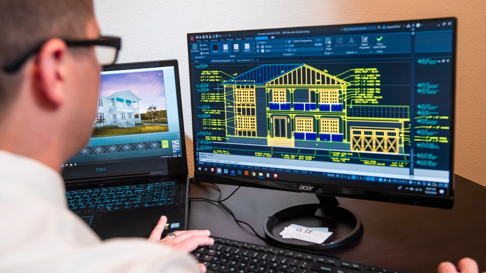 Technical designer reviewing detailed building drawings on computer monitors.